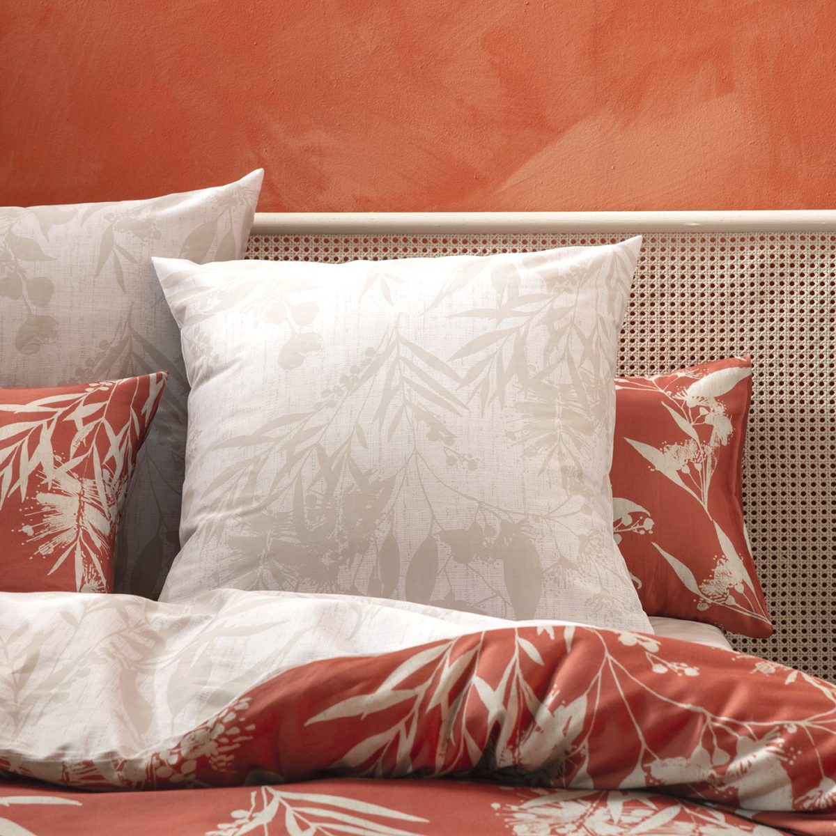 Llit amb roba blanca i estampat floral coral davant d'una paret terracota