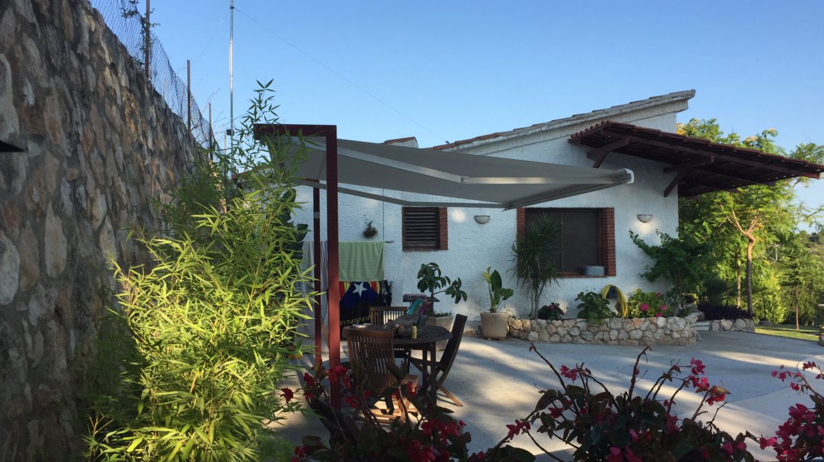 Pèrgola amb tendal davant d'una casa amb jardí
