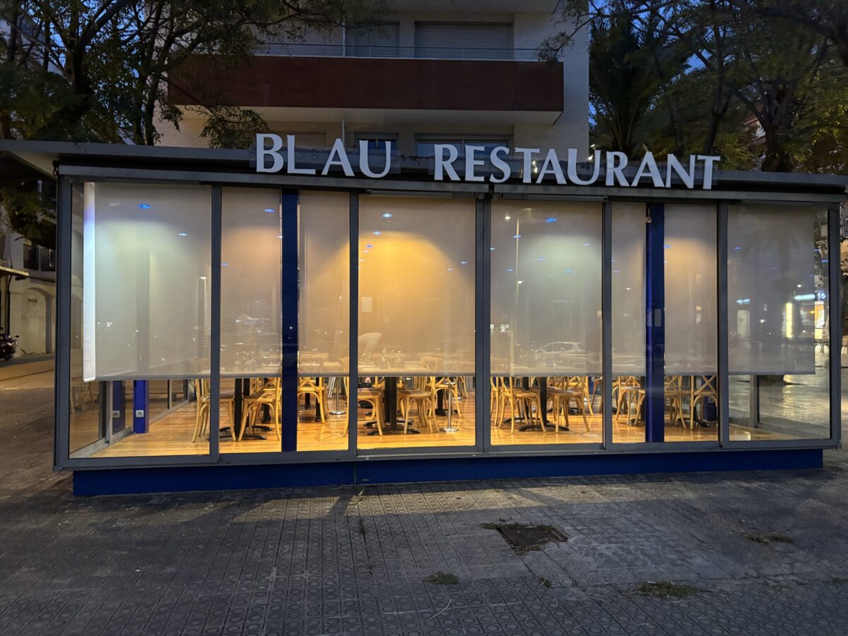 Façana de vidre del restaurant Blau, de nit, amb estors blancs il·luminats per dins