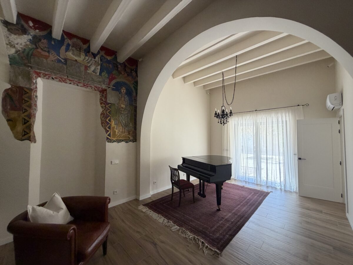 Sala amb arc, piano de cua i cortines de vel blanc a la porta del balcó